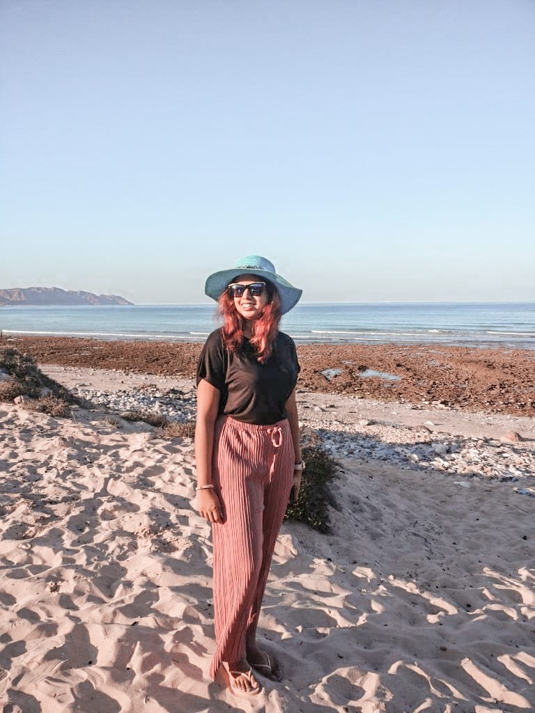 A girl standing on a beach wearing a blue hat and sunglasses